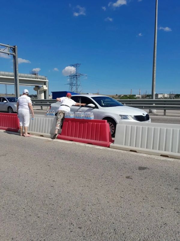 Волонтеры раздают воду людям, стоящим в очереди перед Крымским мостом со стороны Керчи Волонтеры раздают воду людям, стоящим в очереди перед Крымским мостом со стороны Керчи